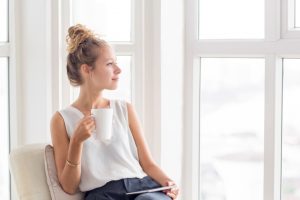 woman with coffee cup sitting next to sunny window